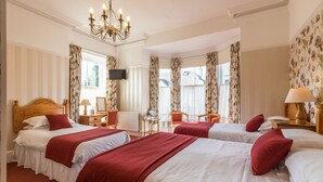 A hotel room with two beds, a TV, a chandelier, and floral wallpaper.
