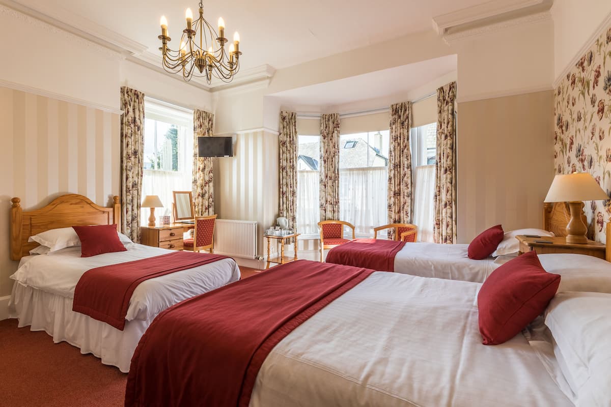 A hotel room with two beds, a TV, a chandelier, and floral wallpaper.