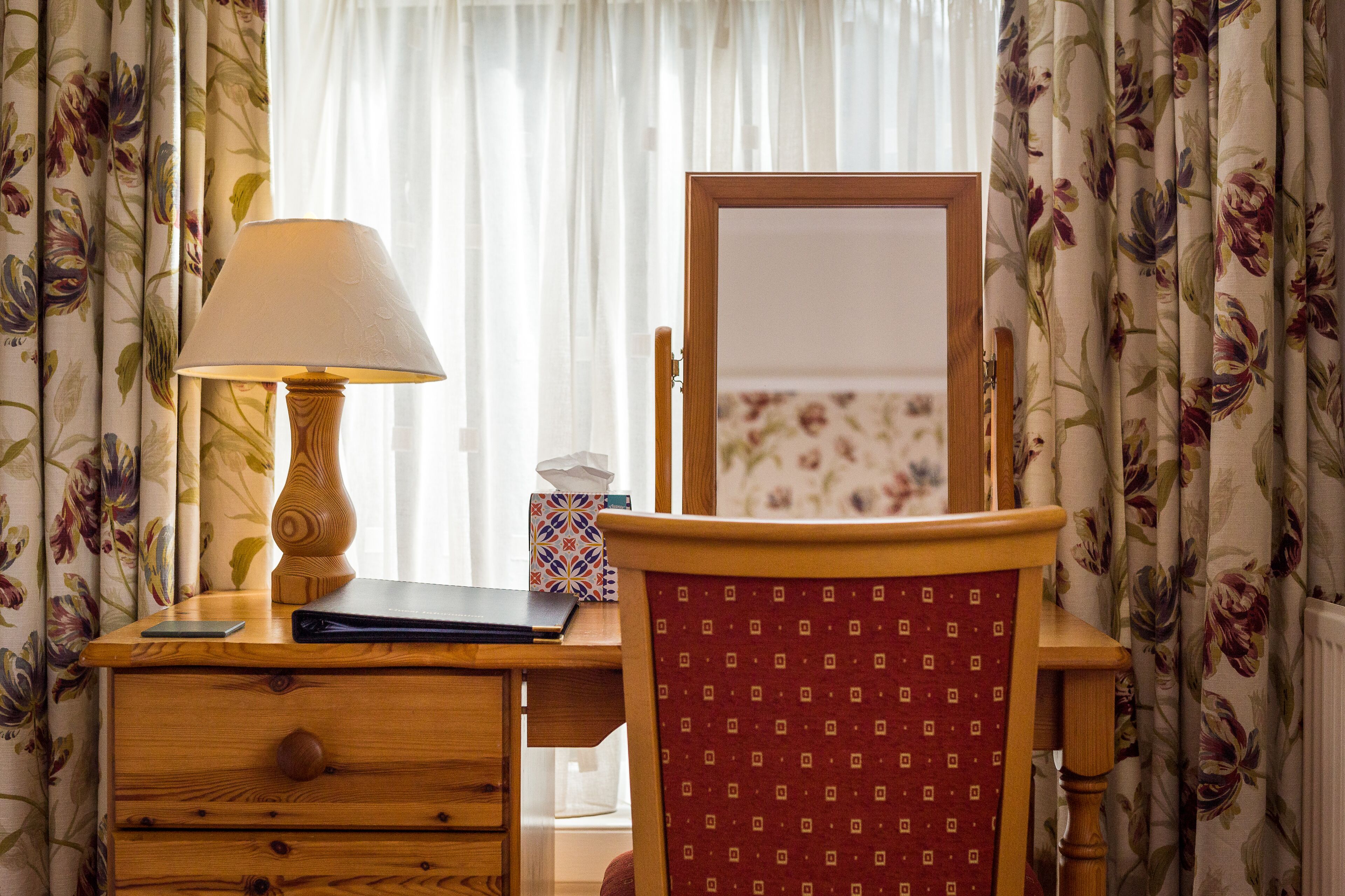 A wooden desk with a lamp, a mirror, and a laptop.