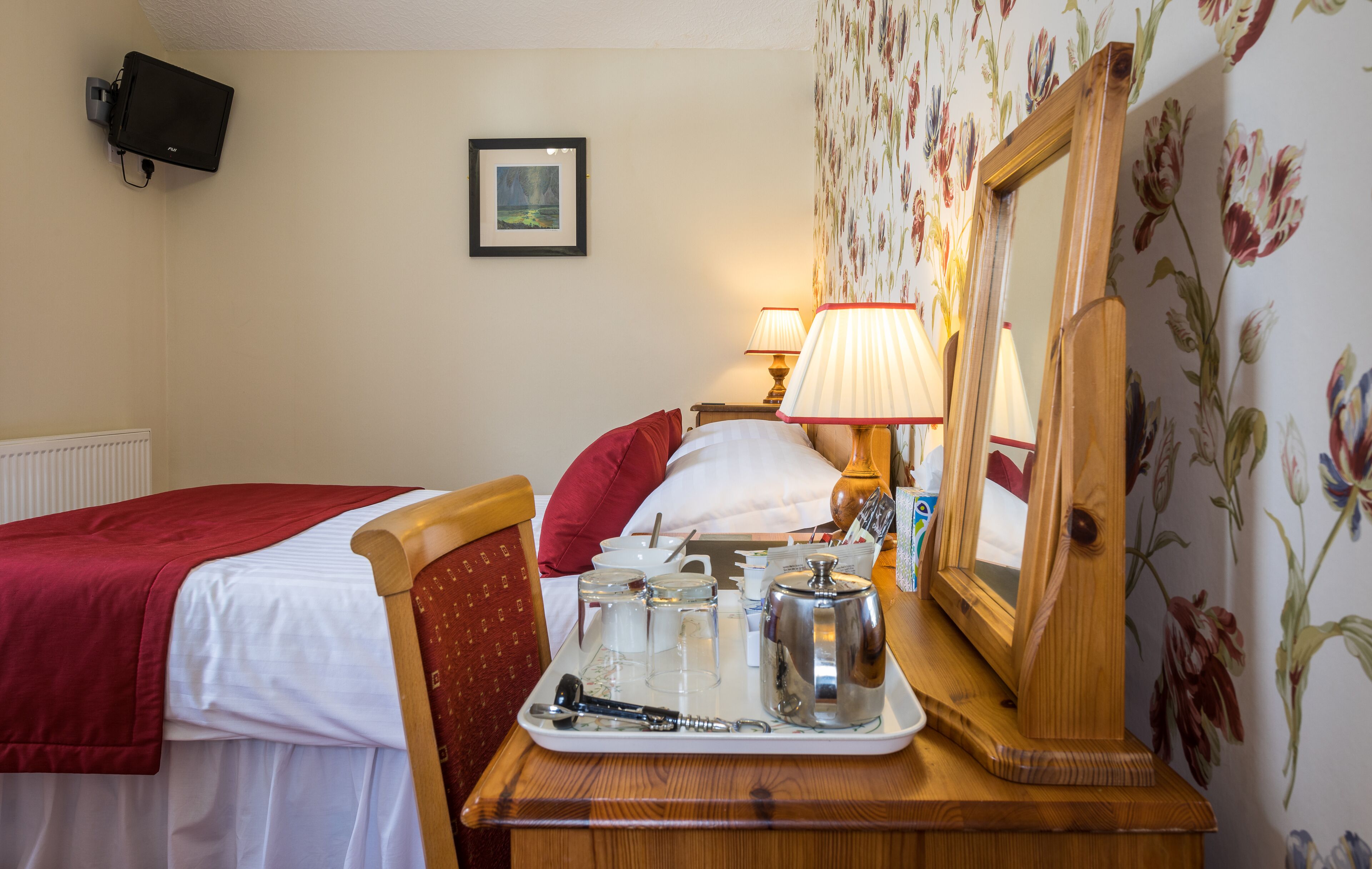 Une chambre d'hôtel avec un lit, une table de chevet sur laquelle se trouve un plateau avec des articles pour le petit-déjeuner, une lampe et un miroir.