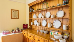 A kitchen area with wooden shelves holding plates, mugs, and a decorative mirror. There are also various kitchen items and a red box on the counter.
