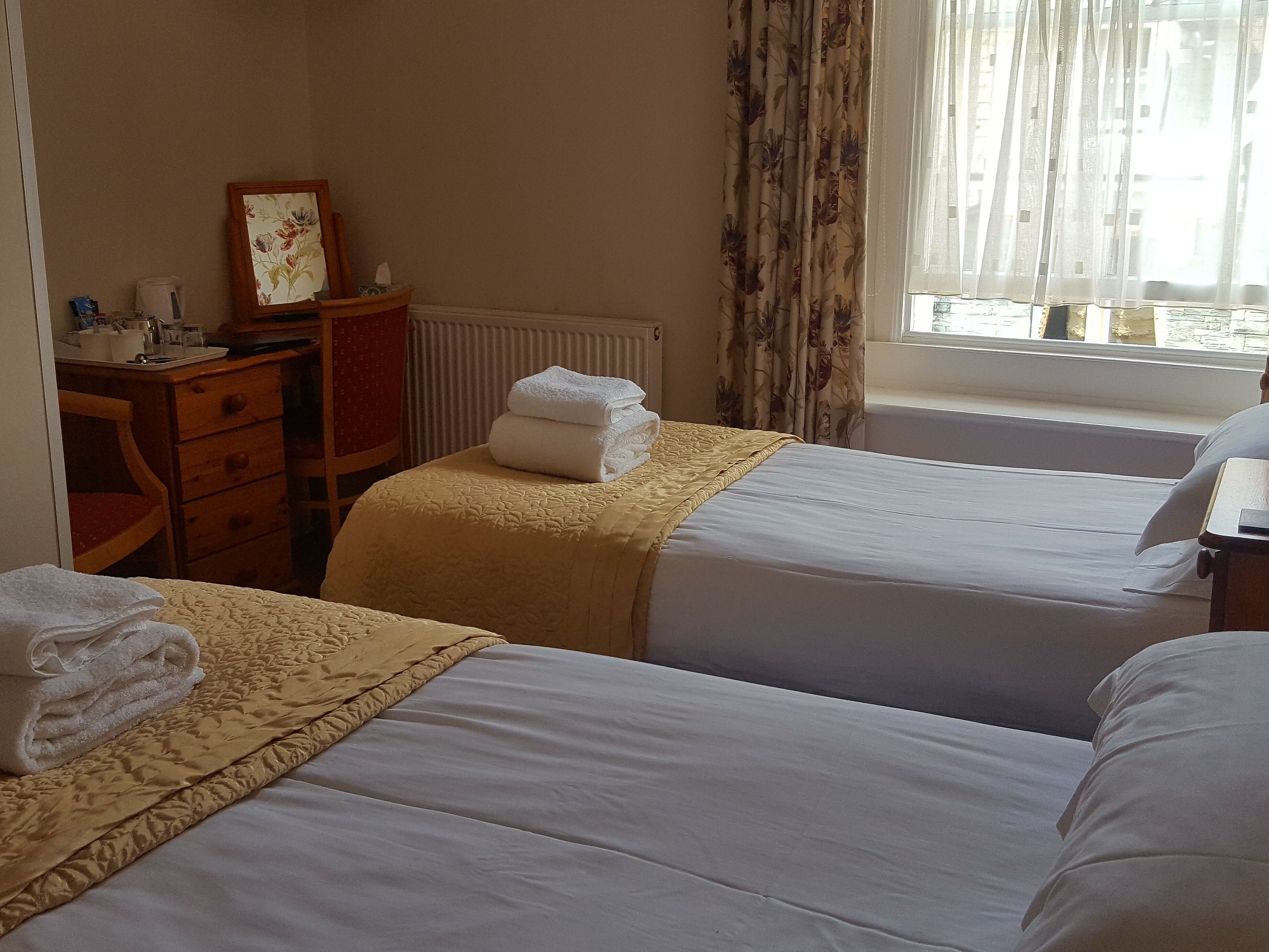 A hotel room with two beds, a wooden dresser, a radiator, and a window with curtains.