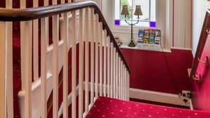 A staircase with a red carpet, white railings, and a window with a view of the outside.
