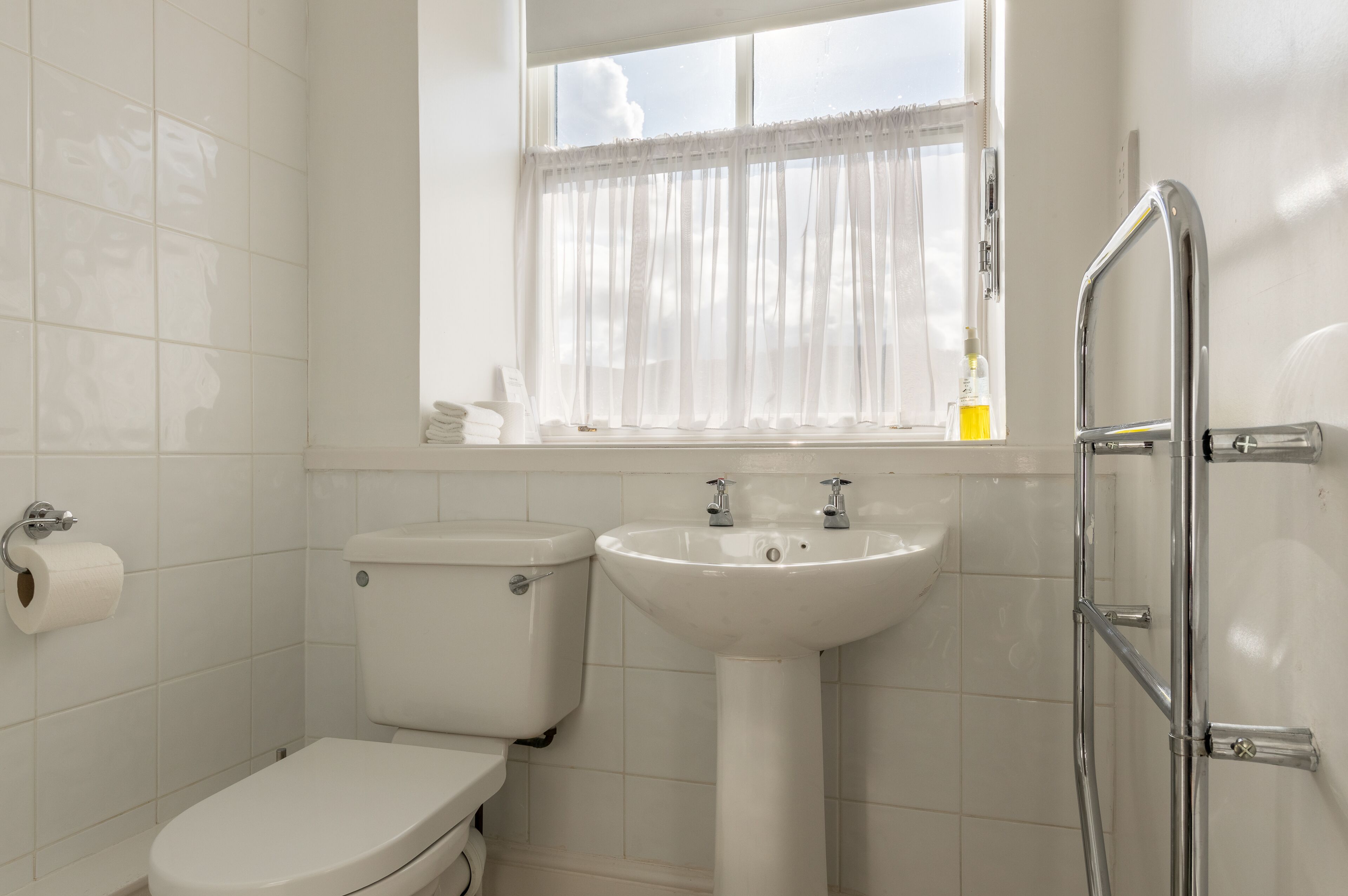 A bathroom with a toilet, sink, and window with curtains.