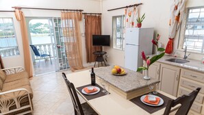 A modern kitchen with a dining area, a TV, and a balcony with a view of the water. - Affordable, Majestic, St. Lucia Jazz and Carnival, Bay View Apartment (Castries)