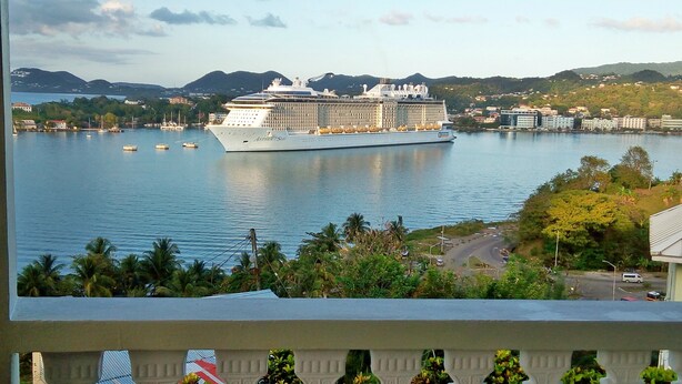 A large cruise ship docked at a port with a mountainous backdrop and a residential area in the foreground. - Affordable, Majestic, St. Lucia Jazz and Carnival, Bay View Apartment (Castries)