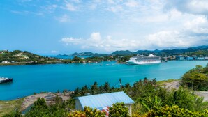A large cruise ship docked at a harbor with clear turquoise water, surrounded by lush greenery and hills in the background. - Affordable, Majestic, St. Lucia Jazz and Carnival, Bay View Apartment (Castries)