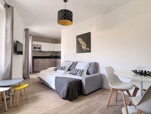 A modern living room with a sofa, dining table, chairs, and a kitchen in the background.