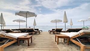 Een strand met houten ligbedden en parasols, een houten looppad naar de zee, en een heldere lucht.