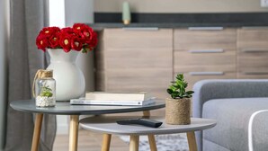 Een moderne woonkamer met een grijze bank, een klein rond tafeltje met een boek, een vaas met rode bloemen, een kleine potplant en een smartphone.