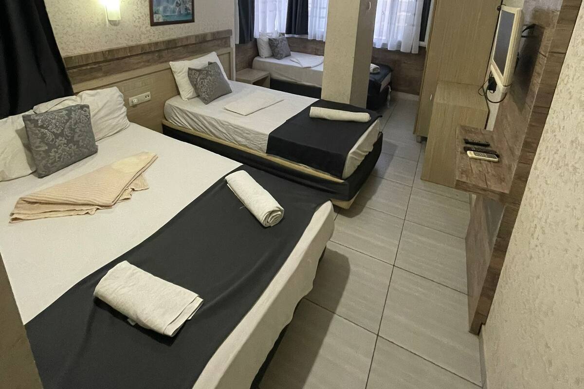 A hotel room with two beds, a TV, a painting, and a window with curtains.
