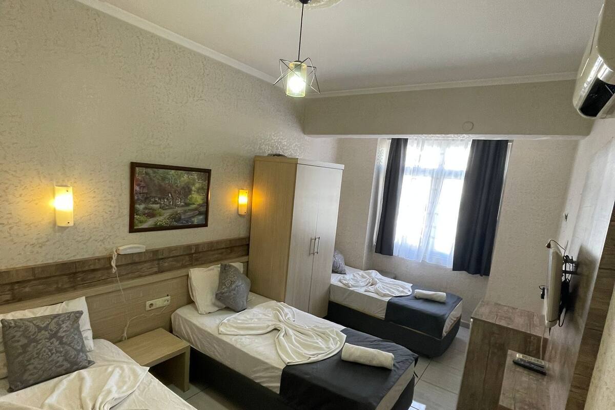 A hotel room with two beds, a wardrobe, a desk with a mirror, and a ceiling fan.