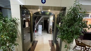 A hotel lobby with a glass entrance, potted plants, a staircase, and a reception desk. - Denizhan Otel (Antalya)