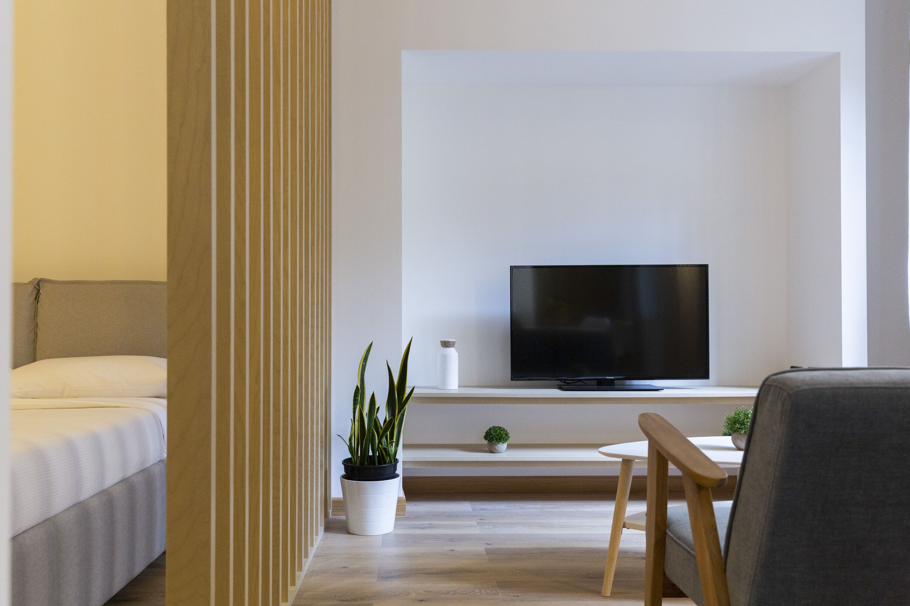 Una habitación de hotel moderna con una cama, un televisor montado en la pared, una mesita con una planta y una silla.