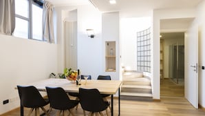 Un comedor moderno con una mesa de madera y sillas negras, una planta pequeña y una botella de vino.
