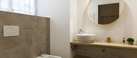 A modern bathroom with a bidet, toilet, sink, and a round mirror.