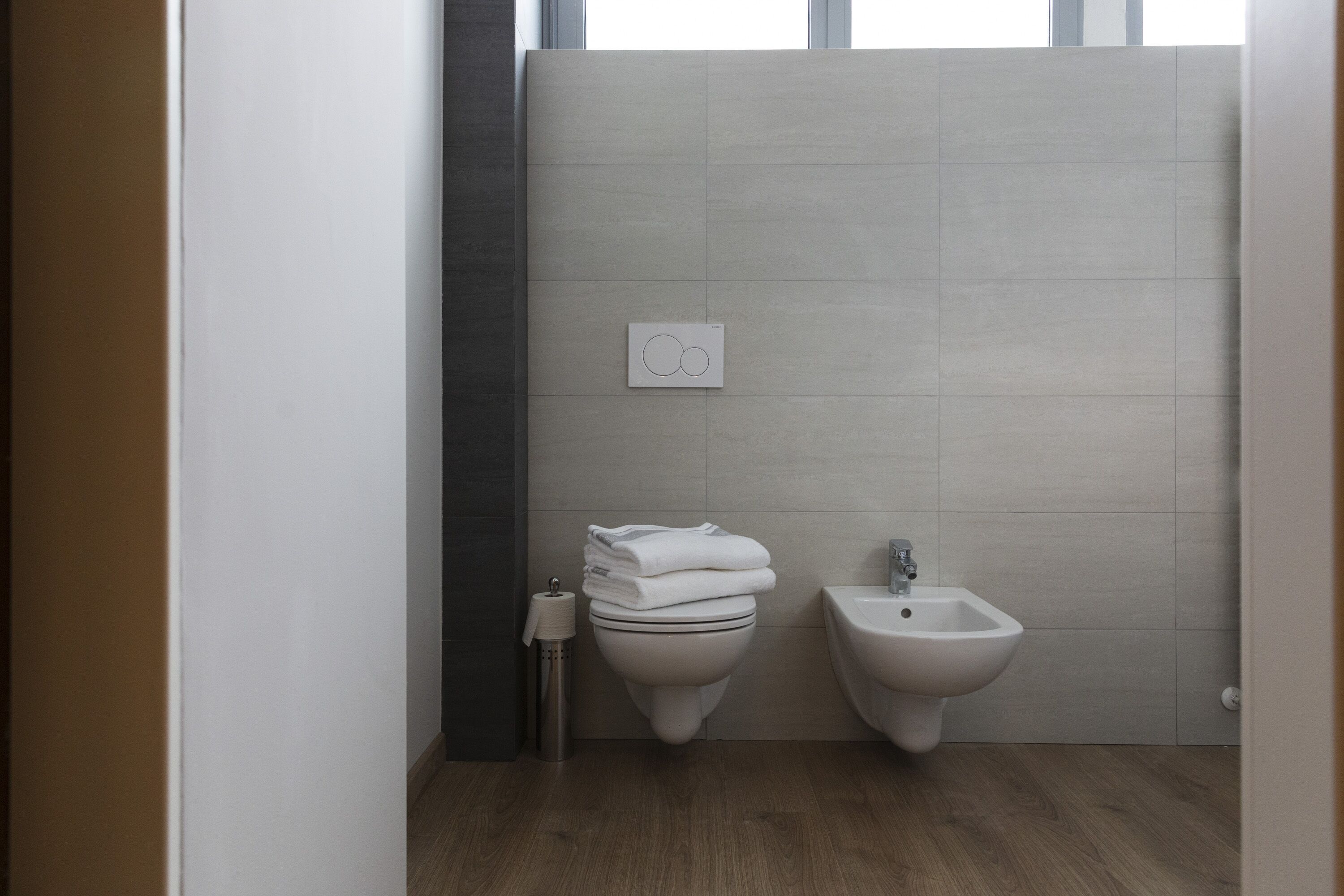 A modern bathroom with a toilet, bidet, and a towel dispenser.