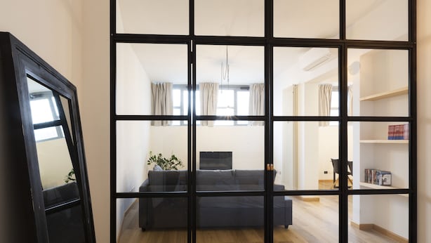 Una habitación con un gran ventanal corredera que da a una sala de estar con un sofá, un televisor y una planta.