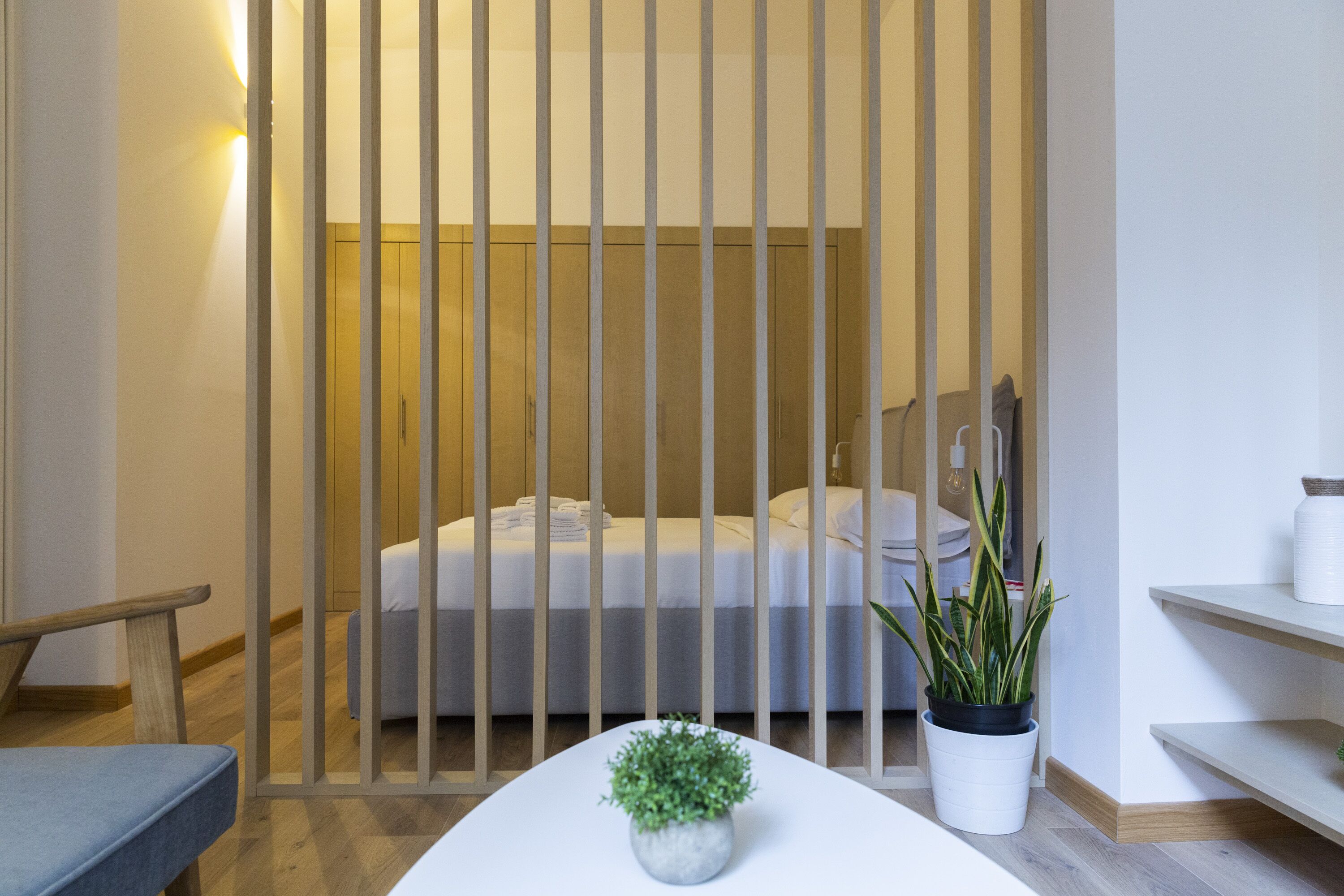 Un dormitori modern amb un llit, una tauleta de nit, una planta en test i una cadira de fusta.