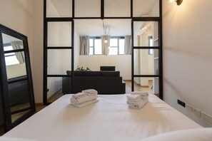 A hotel room with a large bed, a dark sofa, a TV, and a mirror. - notaMi -  Milan Design Flats (Milan)