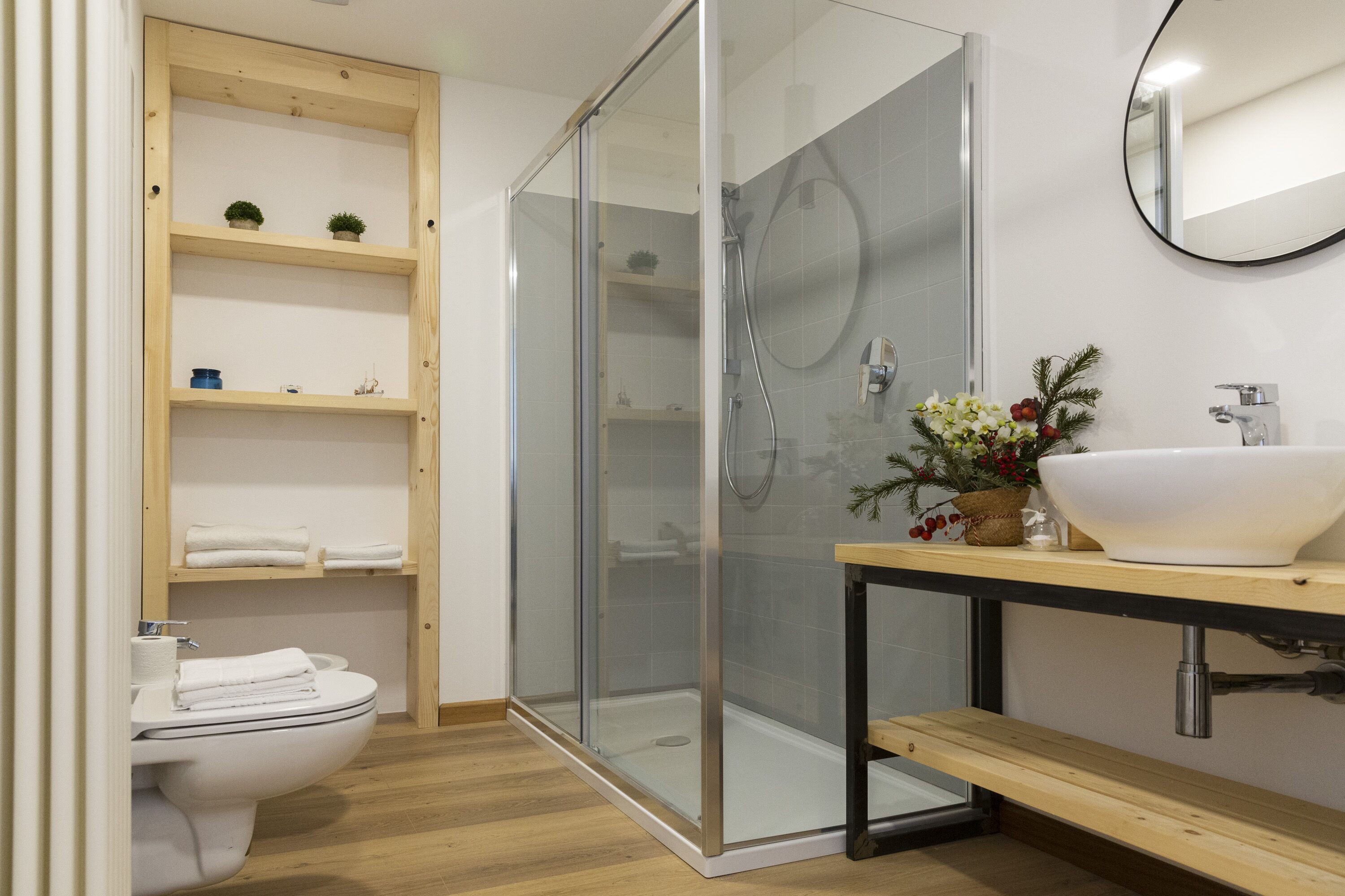 Een moderne badkamer met een douchecabine van glas, een houten wastafelmeubel met een witte wastafel en een toilet met netjes gevouwen handdoeken.