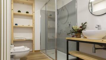 Een moderne badkamer met een douchecabine van glas, een houten wastafelmeubel met een witte wastafel en een toilet met netjes gevouwen handdoeken.