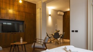 Habitación de hotel moderna con una cama grande, un televisor, un área de comedor y una pared de madera.