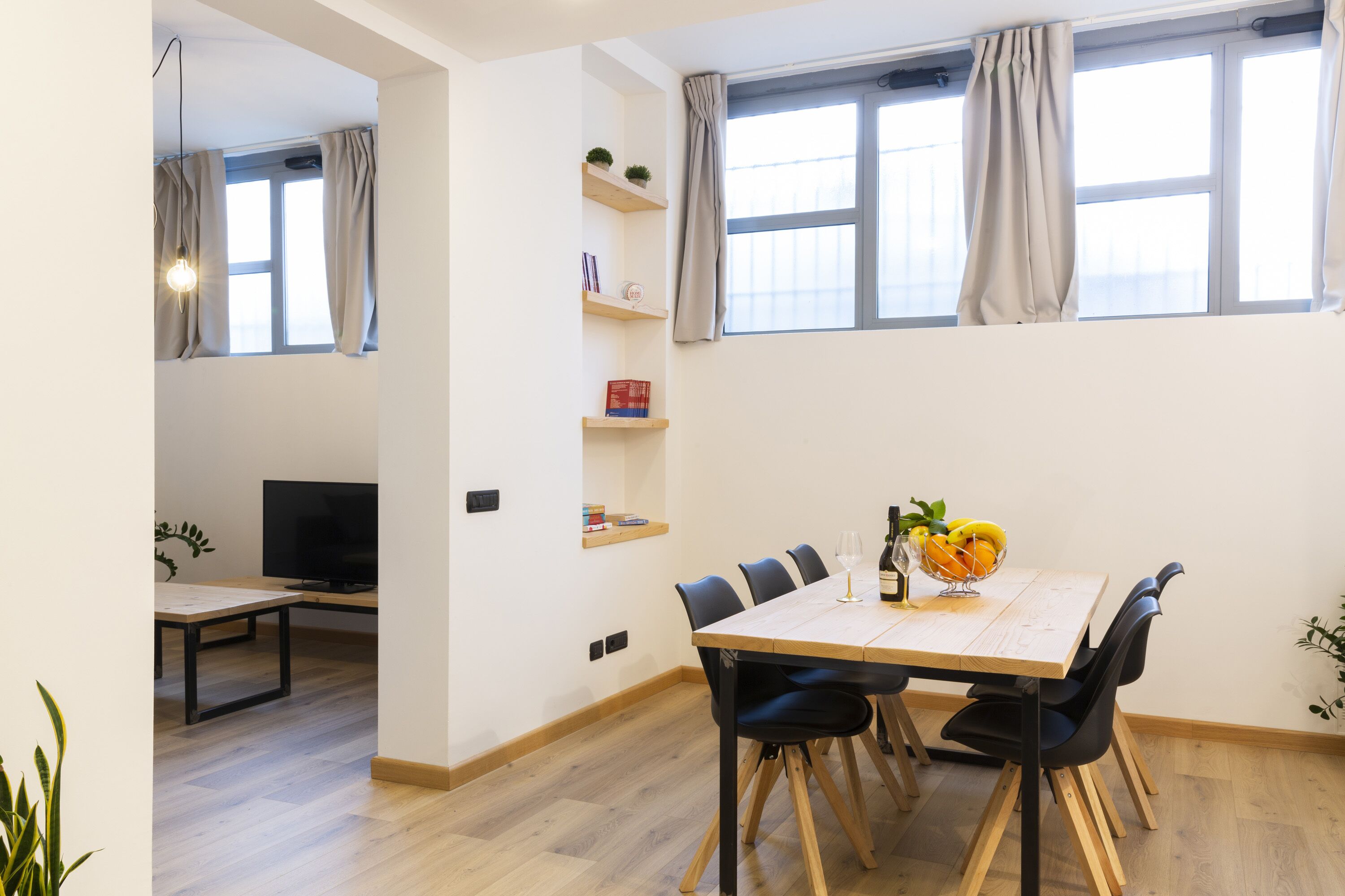 Un coin repas avec une table en bois, des chaises noires et un téléviseur en arrière-plan.