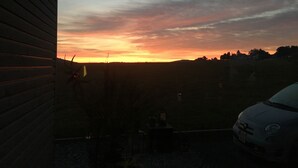 Sonnenuntergangblick aus einem Fenster mit Blick auf ein saftiges Grasfeld, ein Auto im Vordergrund.