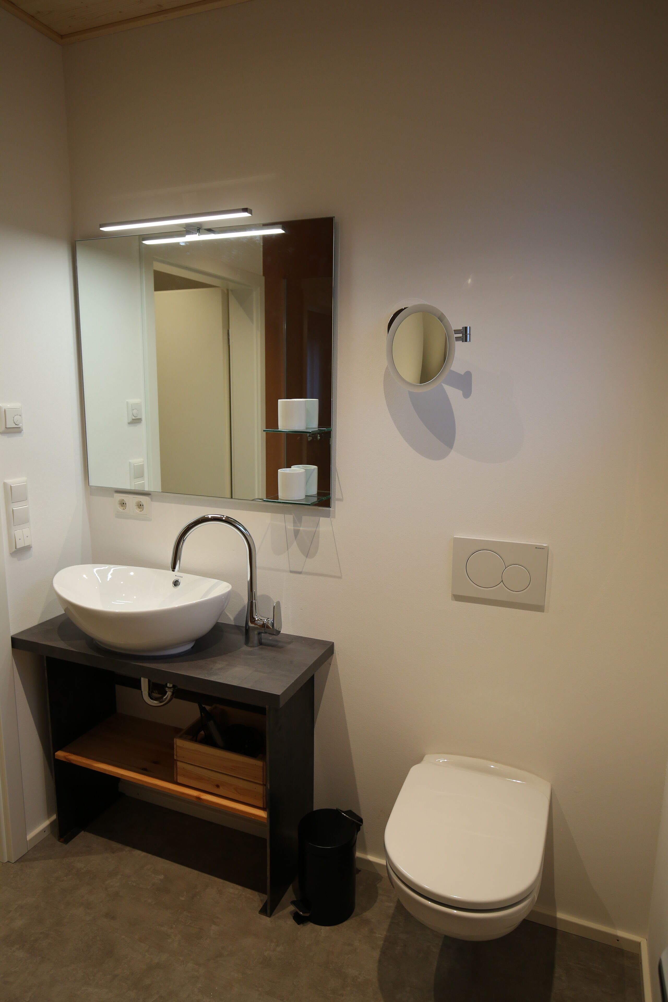 Ein Badezimmer mit Waschbecken, dunklem Waschtisch, Spiegel und Toilette.