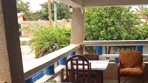 An outdoor patio with a covered seating area, including wooden tables and chairs, and a view of greenery and buildings in the background. - Teley Lodge (Accra)