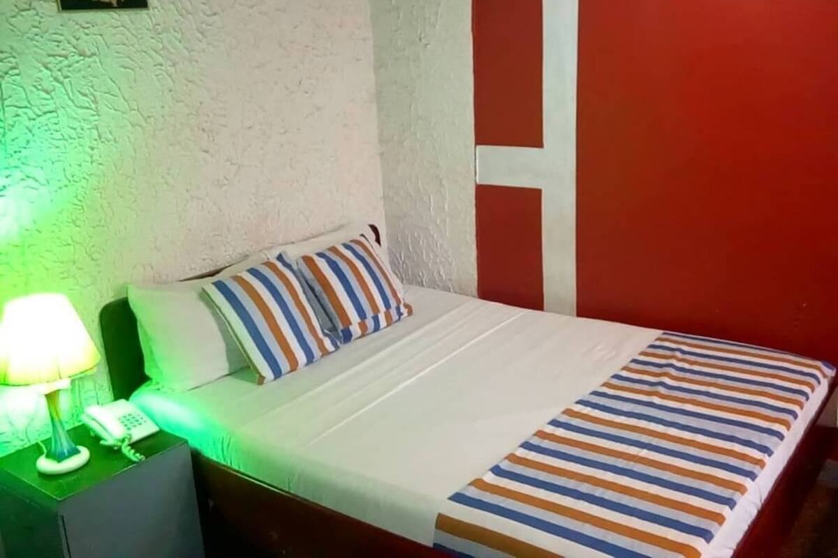 Un lit avec une couvre-lit à rayures, une lampe de chevet et un téléphone sur une table de chevet.