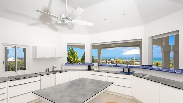 A modern kitchen with a central island, white cabinetry, and large windows offering ocean views.