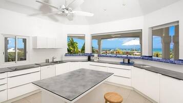 A modern kitchen with a central island, white cabinetry, and large windows offering ocean views.