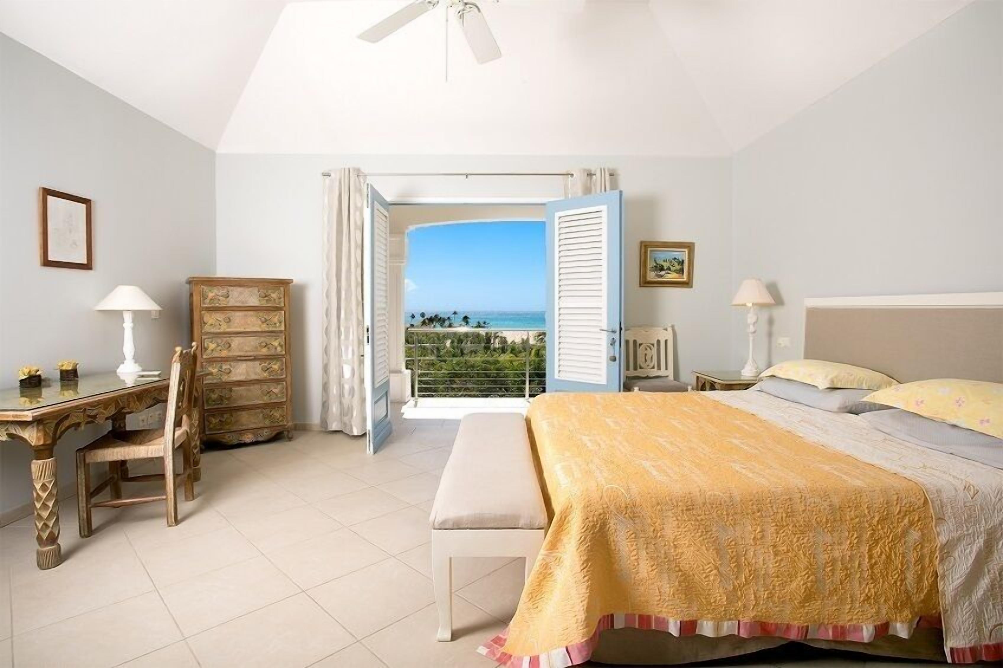 Un dormitorio con cama, escritorio, silla y cómoda. Hay una ventana con vista al océano.