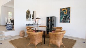 A dining area with a round glass table surrounded by wicker chairs, a black metal side table, and a decorative vase.
