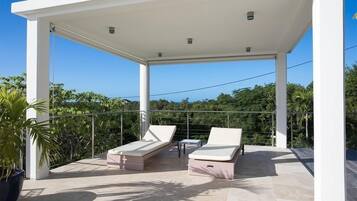 A covered outdoor area with two lounge chairs and a small table, surrounded by a metal railing and potted plants.