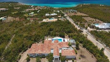 Vista aérea de una propiedad costera con una casa grande, piscina, vegetación densa y una vista despejada del océano.