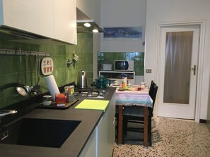 A compact kitchen with a microwave, kettle, and various utensils. A dining table with a chair is positioned near the kitchen.