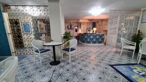 Un vestíbulo de hotel con mostrador de recepción, una mesa redonda con sillas y baldosas de suelo estampadas.