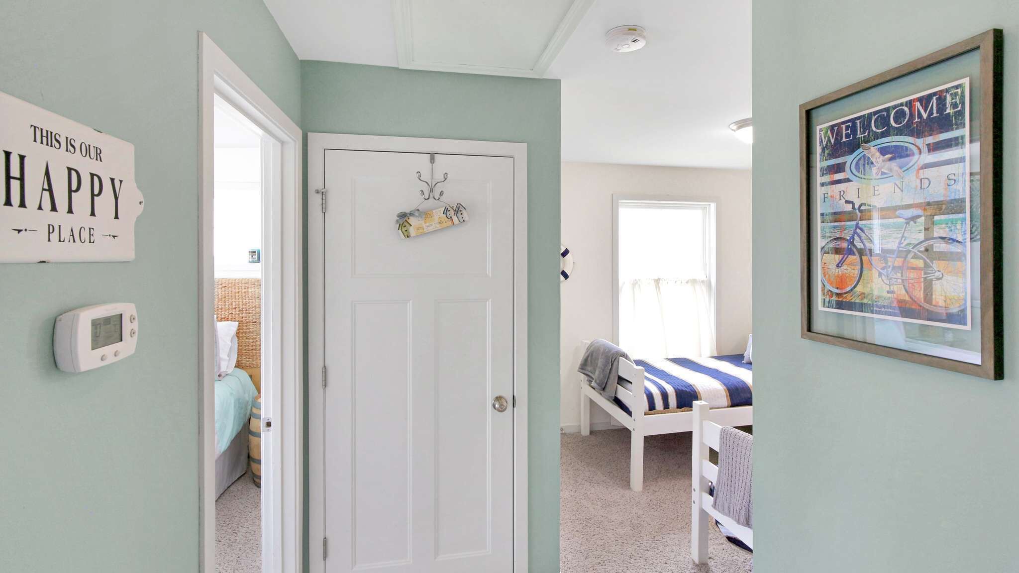 A bedroom with a bed, a door, a thermostat, a welcome sign, and a window.