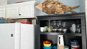 Una cocina con un refrigerador blanco, un adorno de madera y estantes con cristalería y cuencos de colores.