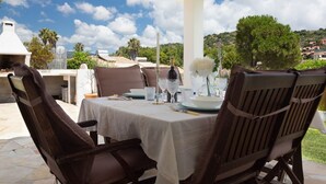 Een terras met eettafel gedekt voor twee personen, omringd door stoelen, een barbecue en uitzicht op het buitengebied.