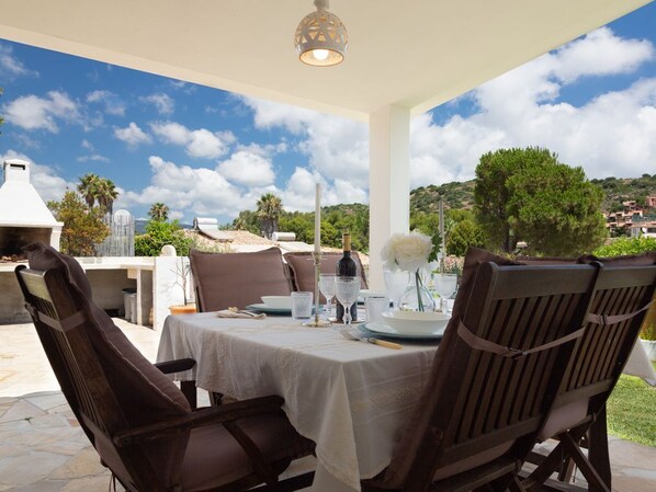 An outdoor dining area with a table set for two, surrounded by chairs, a grill, and a view of the countryside.