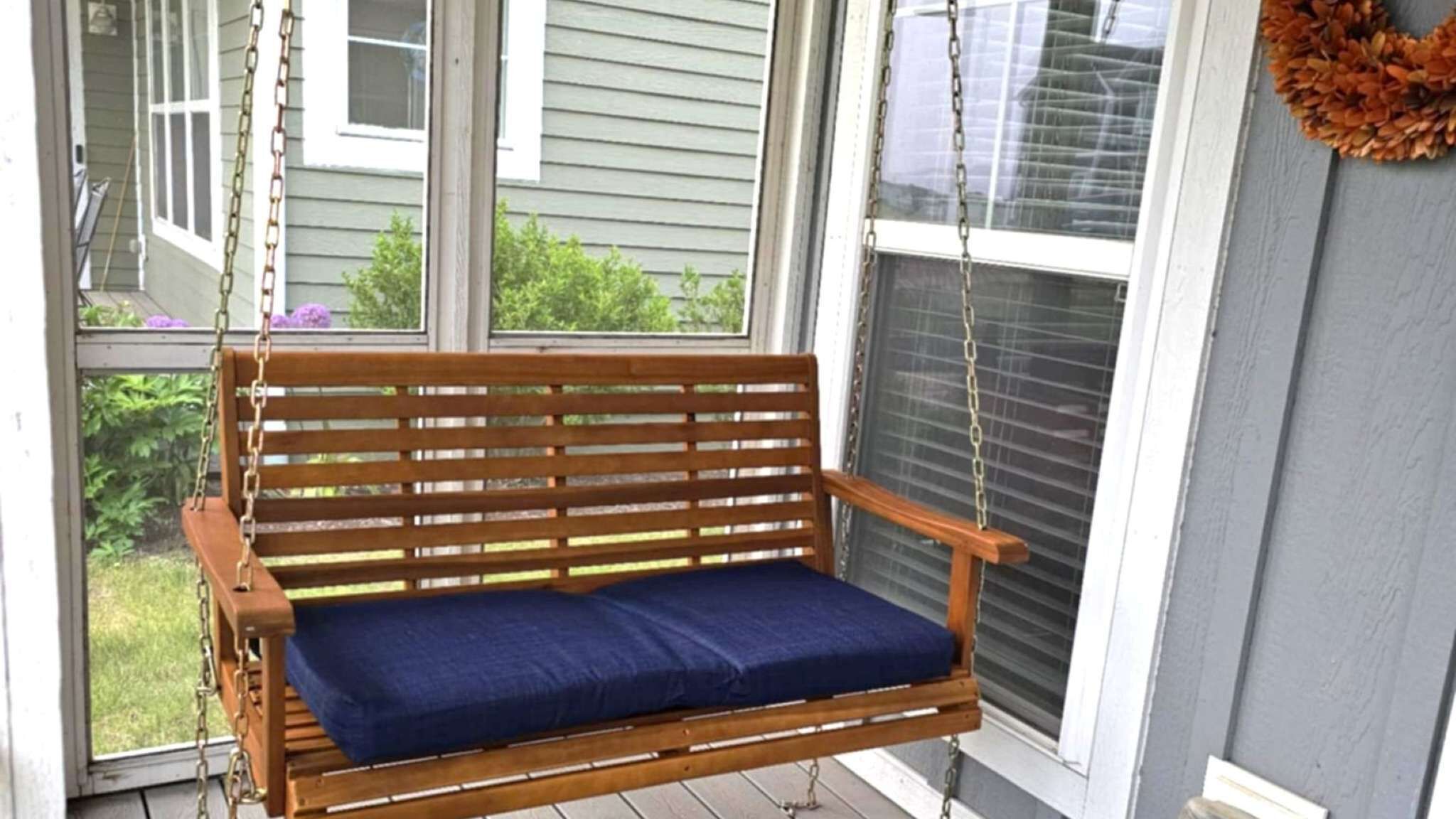 A wooden bench with a blue cushion in a covered porch area with windows.