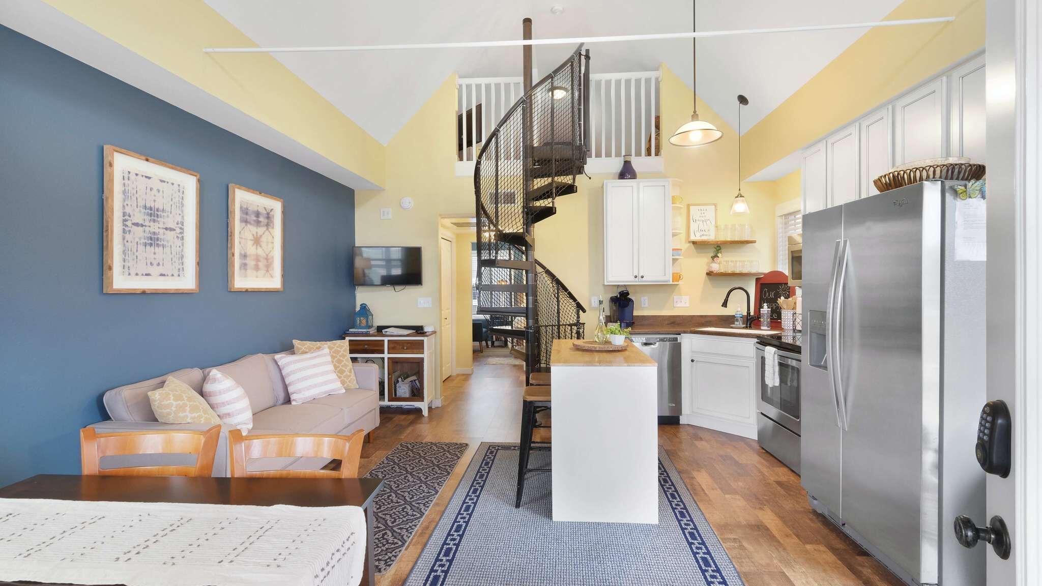 A compact living space with a sofa, a dining area, a kitchen with a refrigerator, and a staircase.