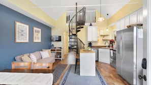A compact living space with a sofa, a dining area, a kitchen with a refrigerator, and a staircase. - Panoramic Views of the Illinois Waterway (Ottawa)