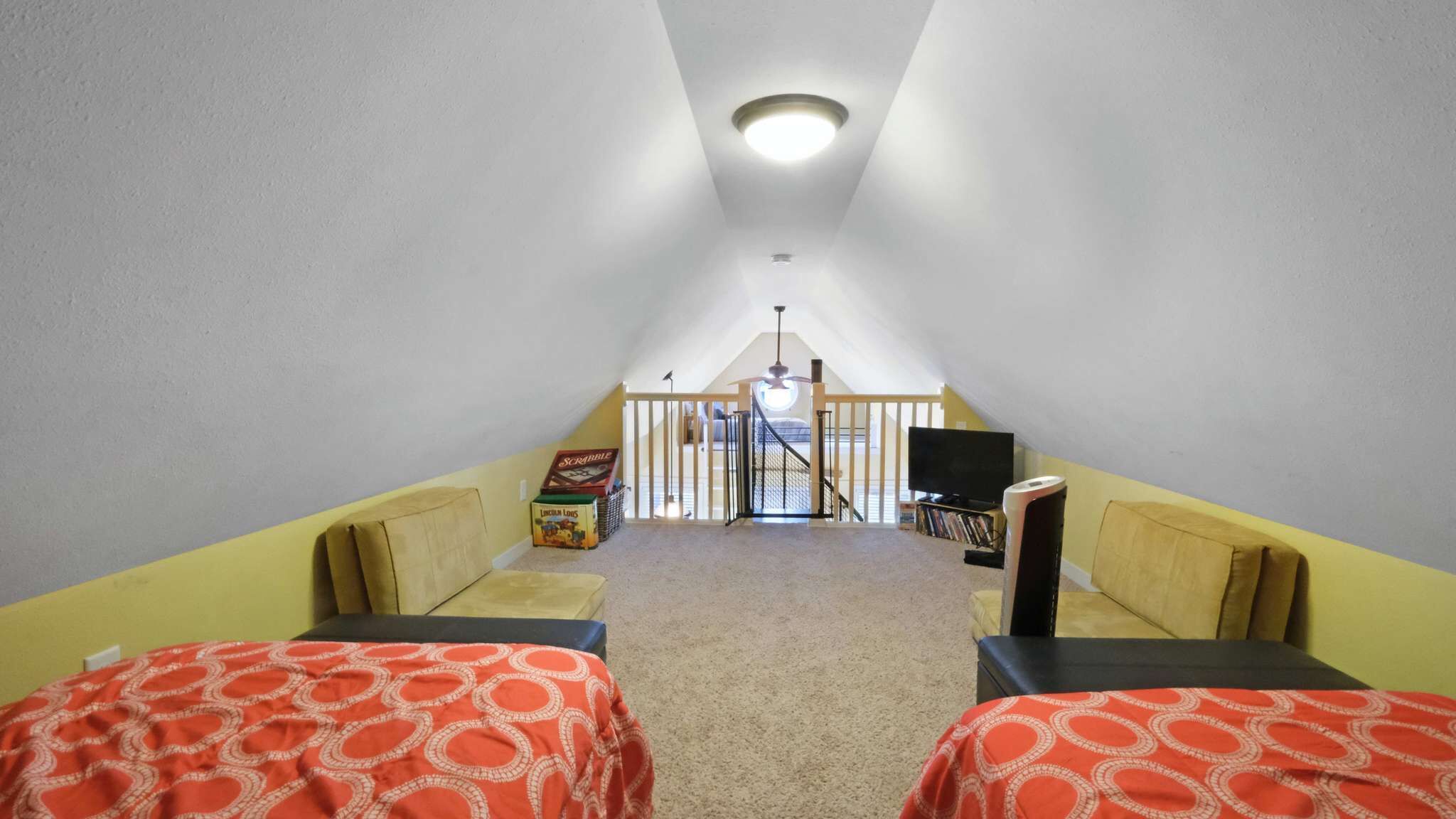 A room with two beds, a TV, a bookshelf, and a staircase leading to an upper level.