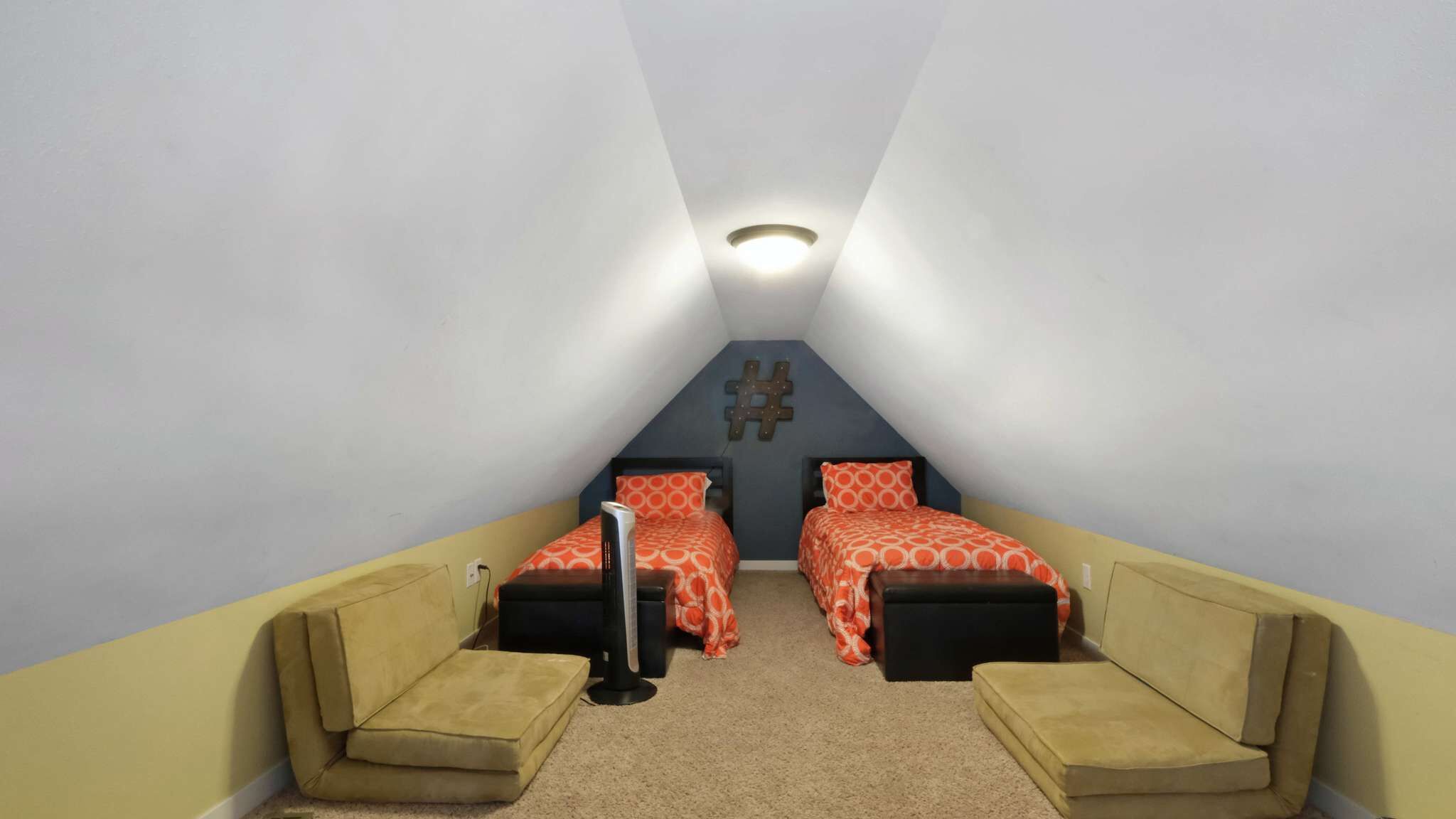 A small, triangular attic bedroom with two beds, a desk, and a chair.