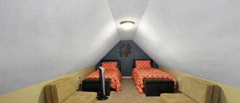 A small, triangular attic bedroom with two beds, a desk, and a chair.
